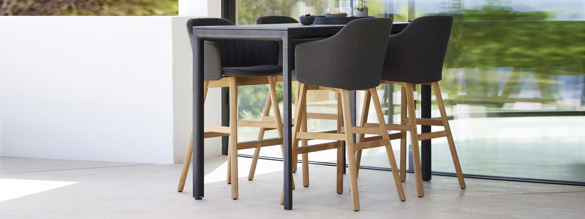 Image of Choice modern outdoor bar chairs with FSC teak legs and 100% recycled polypropylene shell, together with Drop bar table by Cane-line