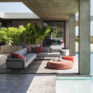 Image of RODA Estendo modern Italian garden sofa and Double round garden poufs, shown beneath modern concrete pergola with exotic plants in the background and swimming pool to the right-hand side.