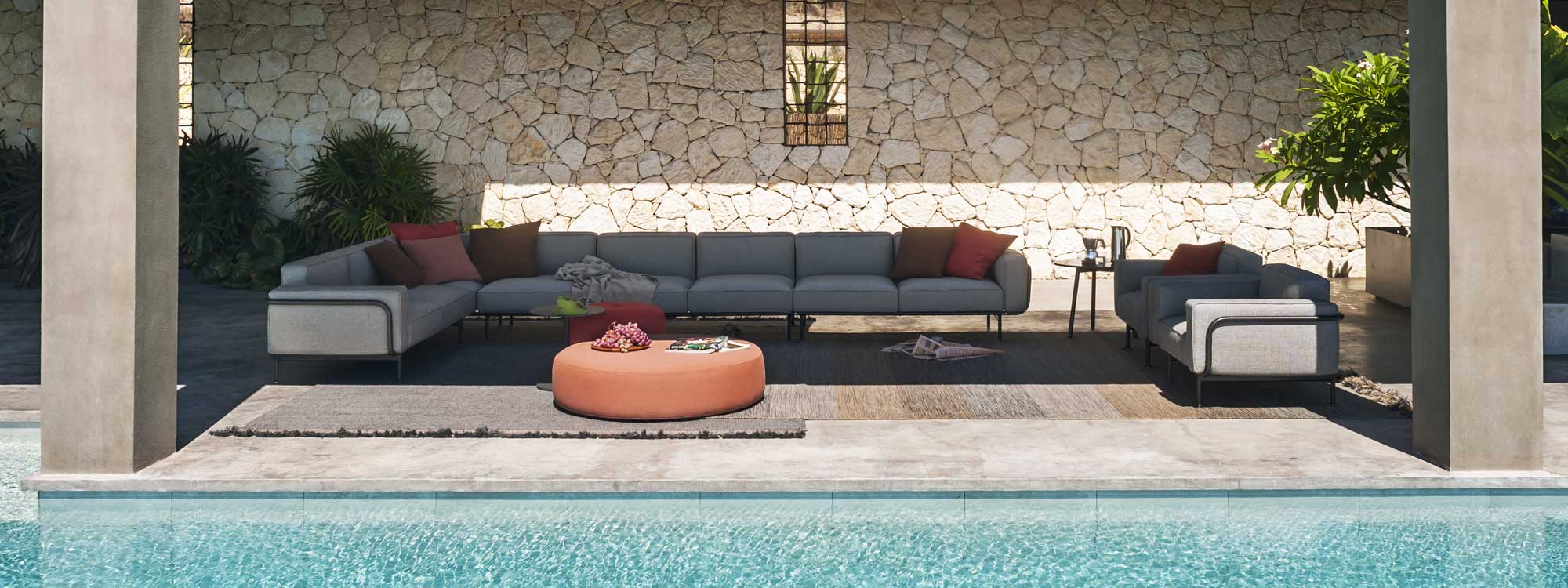 Image of Estendo large outdoor corner sofa and lounge chairs and Double circular garden pouf by RODA, shown on poolside terrace in the shade