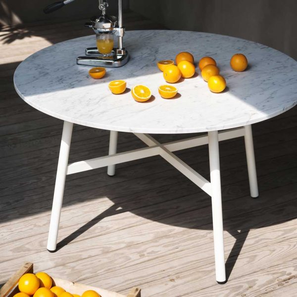 Image of RODA Gamma modern round outdoor table in carrara marble and white stainless steel, with loose oranges and orange press on the table top