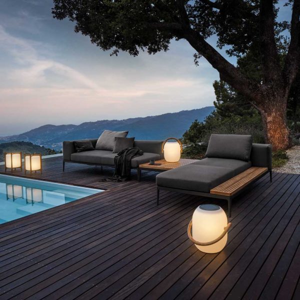 Image at dusk of Gloster Grid sofa and chaise longue on poolside with illuminated Cocoon lanterns.