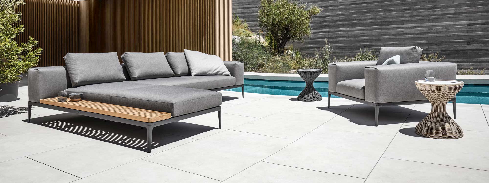 Image of Grid minimalist garden sofa and lounge chair in Meteor grey with grey cushions by Gloster, in sunny courtyard next to swimming pool