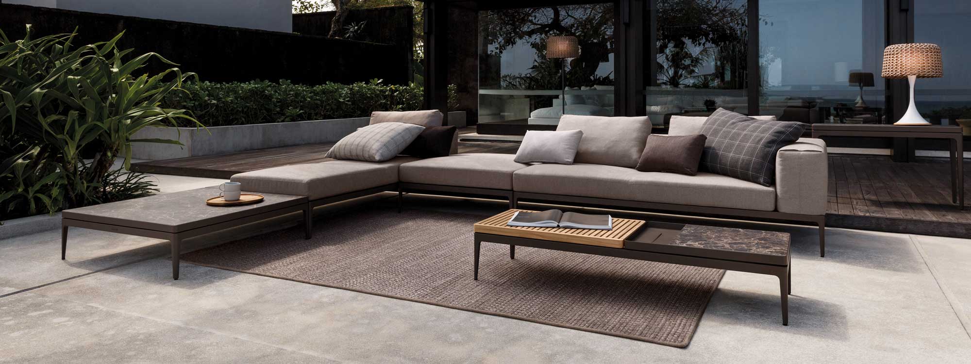 Image of Grid large modern garden sofa with grey frame and cushions, and table surfaces in teak and ceramic by Gloster
