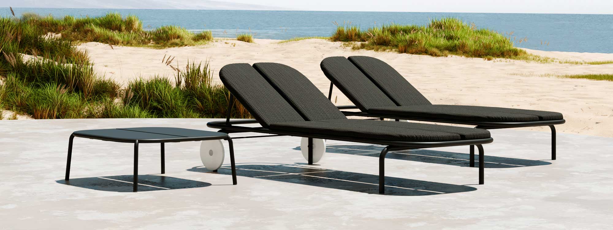 Image of pair of Oiside Parc contemporary tubular aluminium sun loungers and a low table, with sand dunes and sea in the background