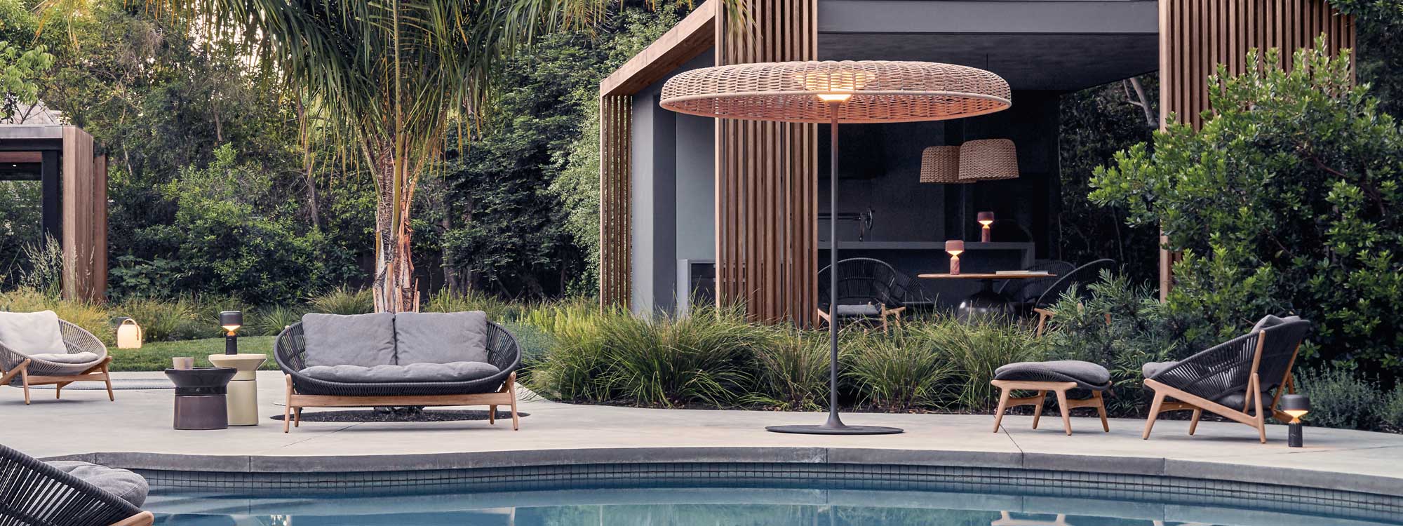 Image of illuminated Ambient Sol parasol lantern on poolside next to Bora lounge sofa by Gloster