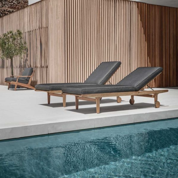 Image of Gloster Bay modern teak sunbed on sunny poolside terrace with wooden clad building in the background