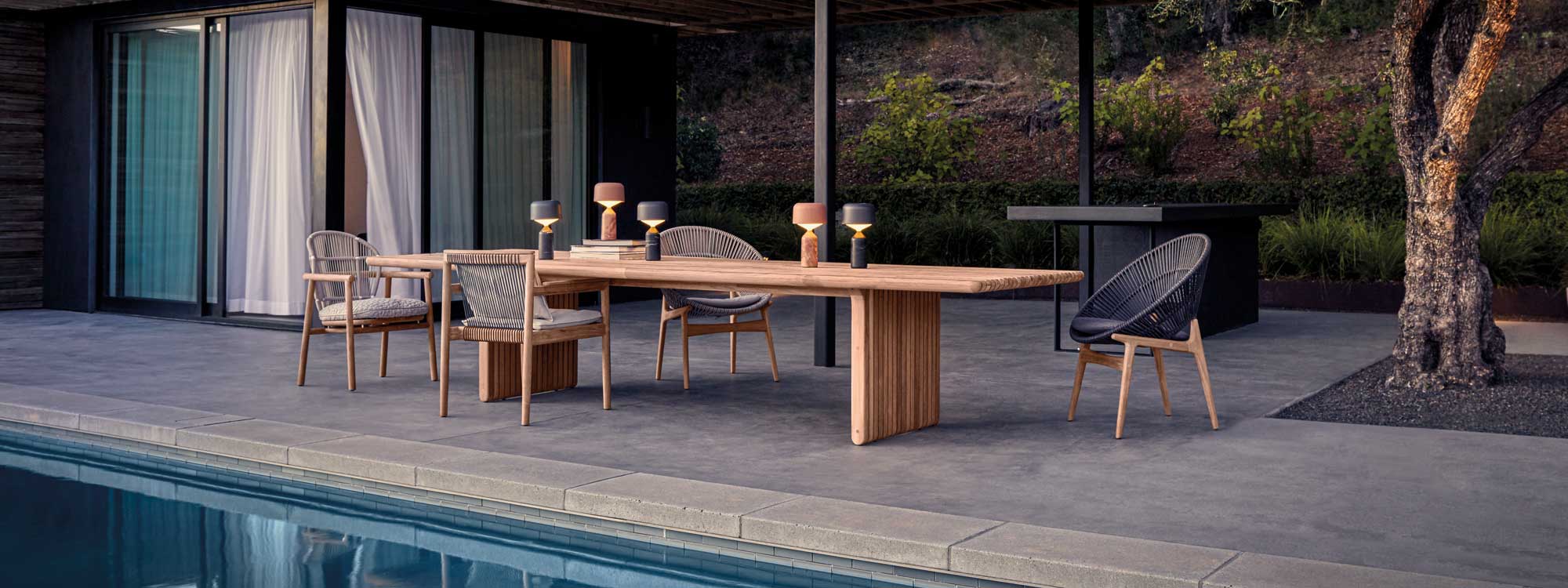 Image of Gloster Deck linear teak table on poolside with different Gloster garden chairs