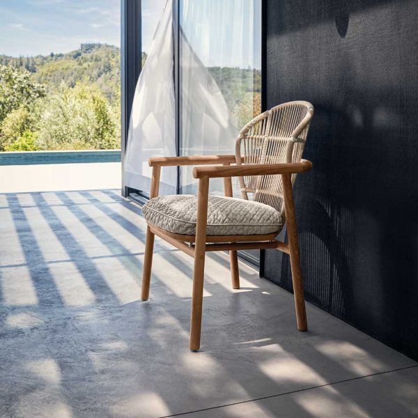 Image of Gloster Fern teak dining chair with plump seat cushion, in shade of terrace with swimming pool and rolling hills in the background