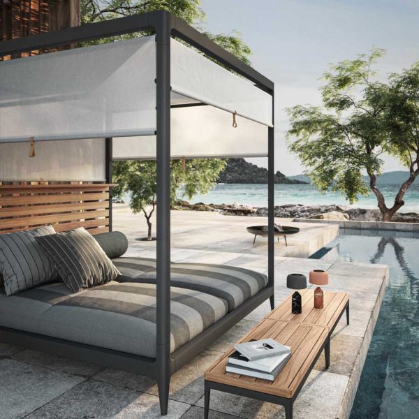 Image of Gloster Grid Cabana daybed with roof and adjustable screens, with swimming pool to the side and sea in the background