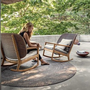 Image of pair of Gloster Kay modern rocking chairs with teak frames and all-weather wicker backs, in sun and shade of outdoor balcony