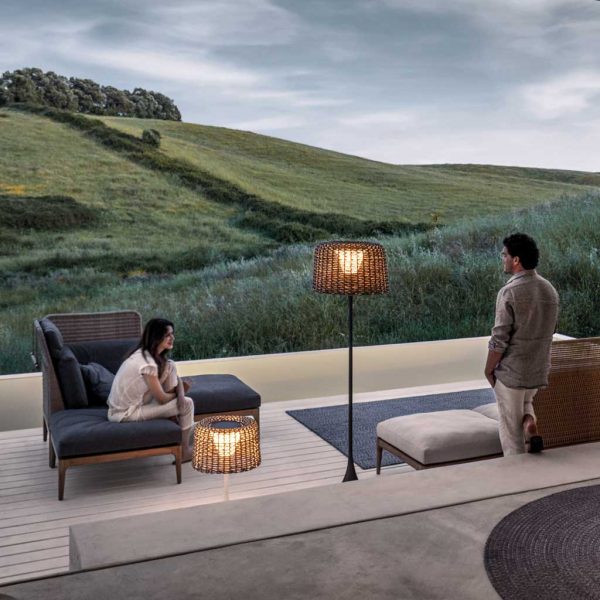 Image of couple relaxing around Gloster Lima luxury wicker garden furniture on terrace with undulating countryside in the background