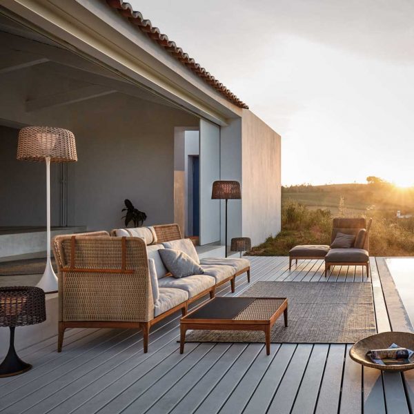 Image at sunset of Gloster Lima modular rattan garden sofa on wooden decked terrace next to swimming pool