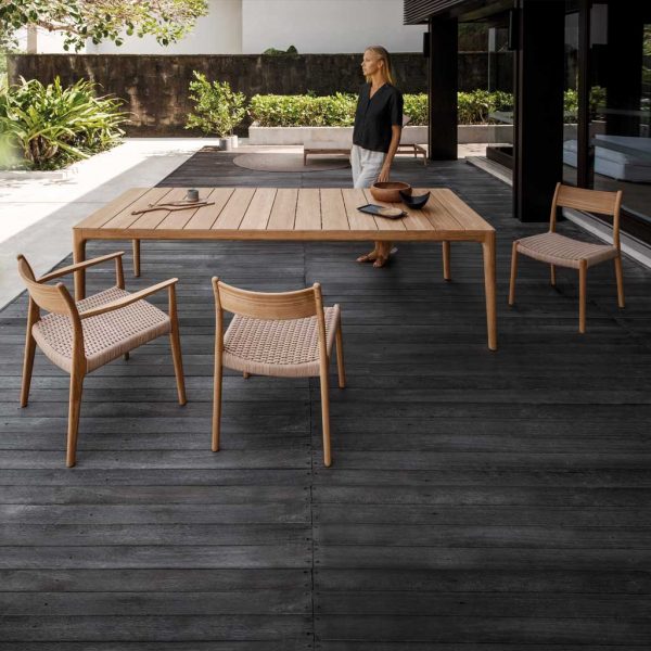 Image of woman stood next to Gloster Lima teak dining table and chairs on covered wooden decking