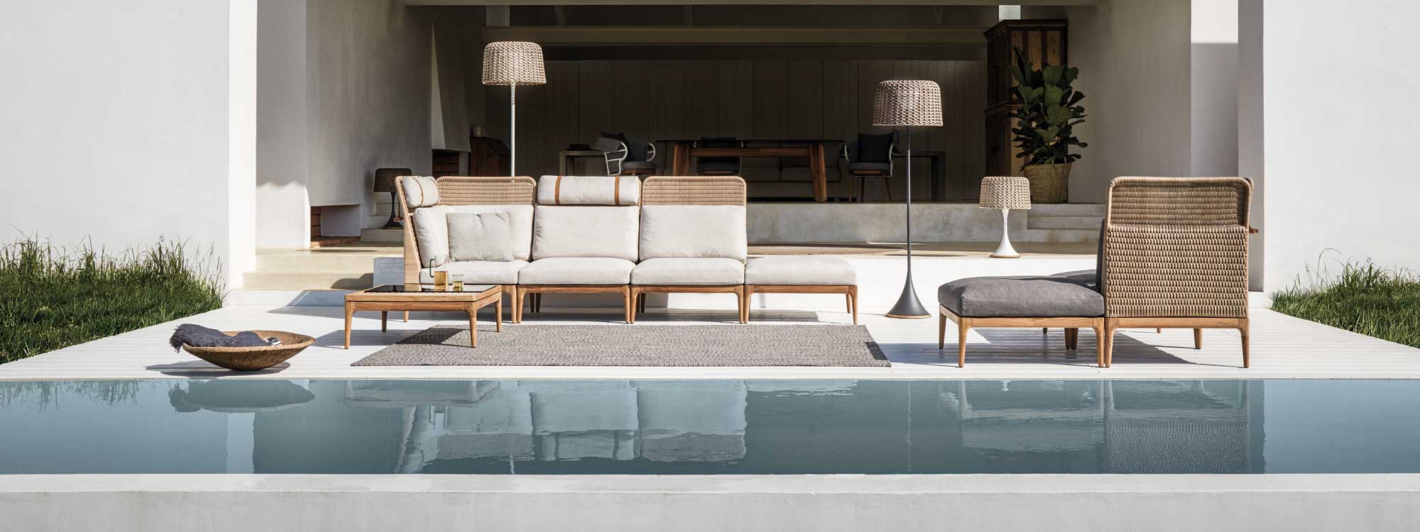 Image of Gloster Lima modern cane garden sofa with teak base , together with Mesh outdoor floor lamps on a minimalist poolside