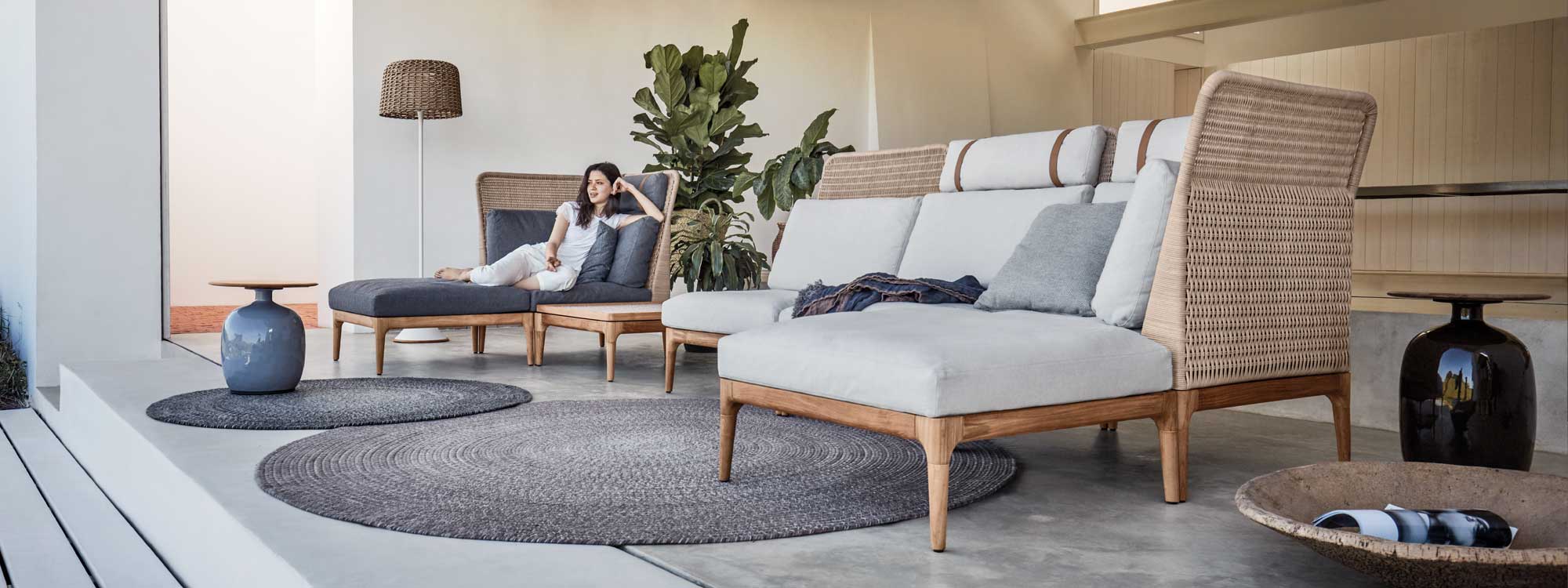 Image of woman lying back in Lima luxury rattan daybed next to Lima garden sofa and Blow side tables