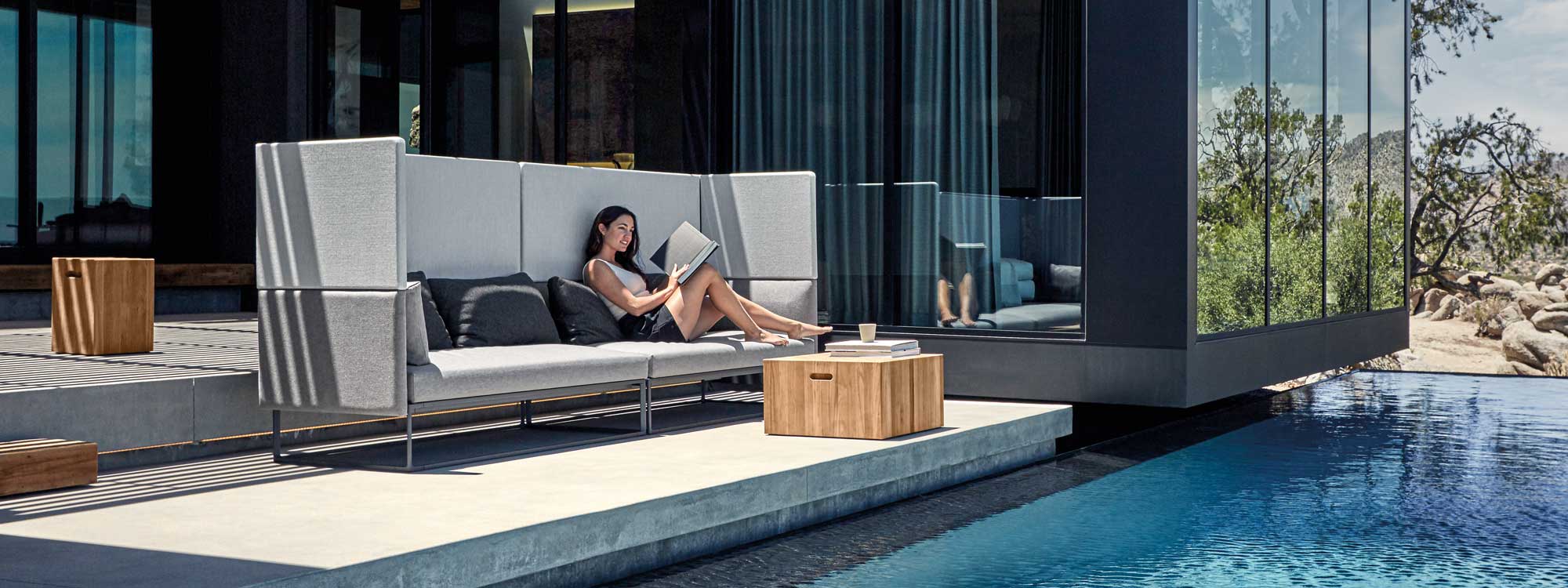 Image of woman sat reading on Maya Cove high backed garden sofa by Gloster next to Block low table