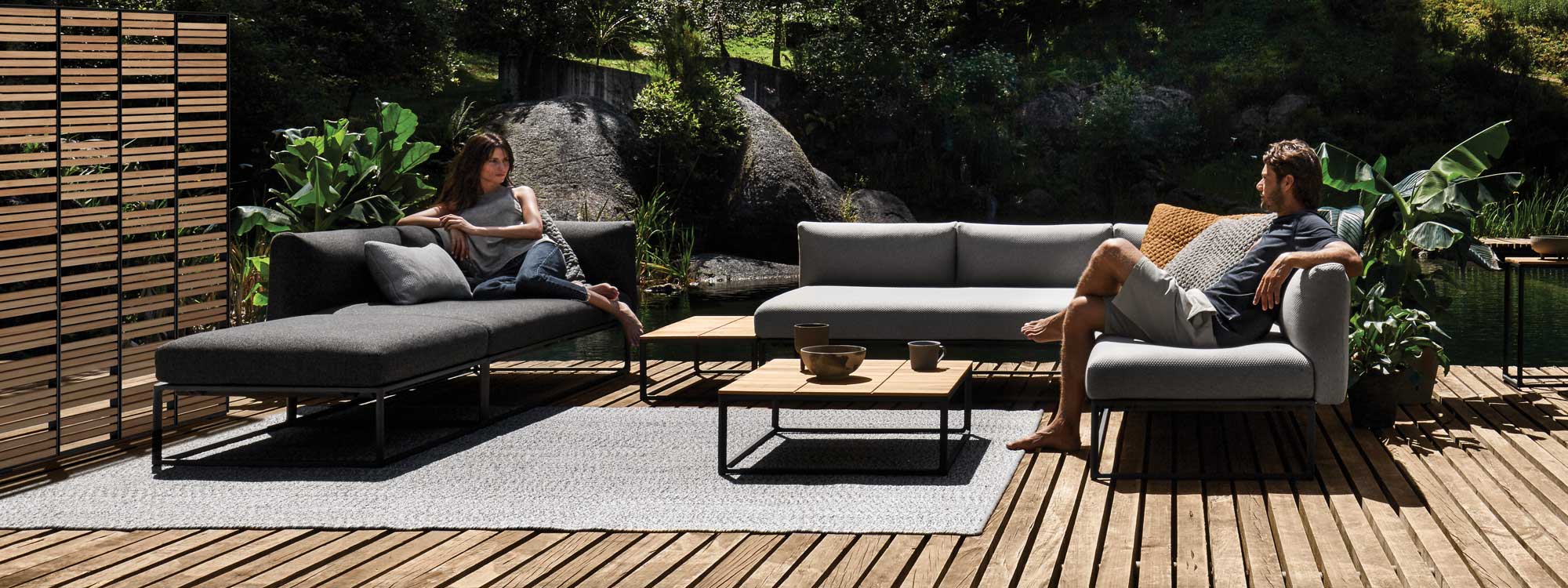 Image of couple relaxing on Gloster Maya luxury garden corner sofa and daybed, with teak and meteor-coloured Screen in the background