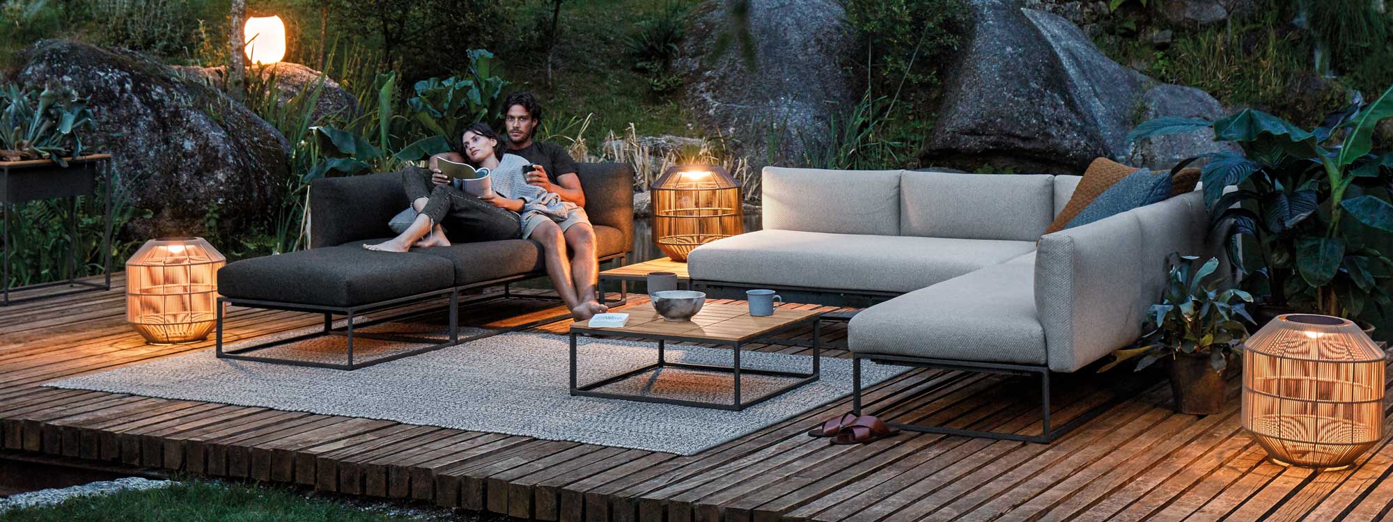 Image at dusk of couple snuggling together on Gloster Maya luxury garden sofa, punctuated by Nest garden lights
