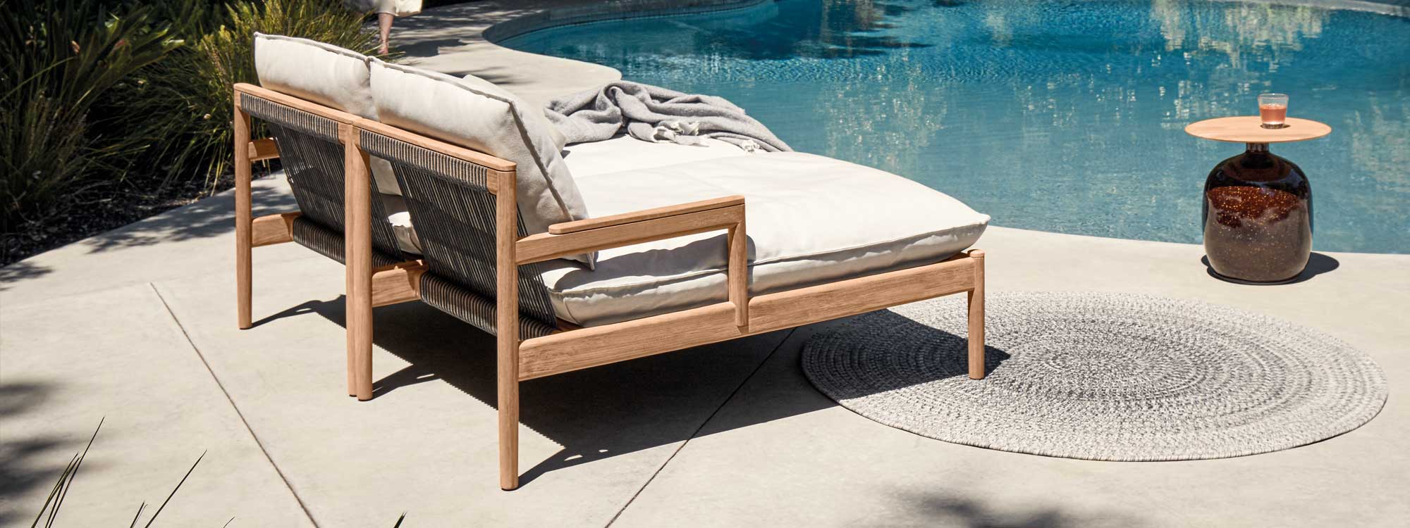 Image of pair of Gloster Saranac teak daybeds with black all-weather rope, placed side to side next to Blow side table