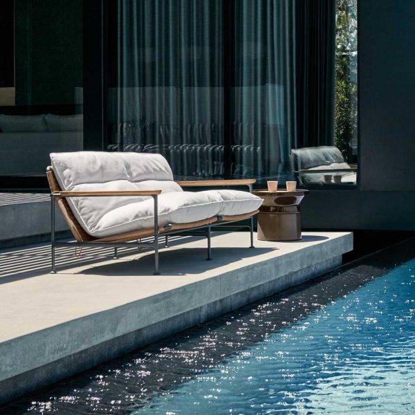 Image of Gloster Zenith 2 seater garden sofa with white cushions alongside rippled waters of swimming pool