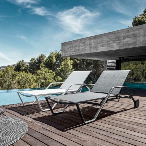 Image of pair of Gloster 180 modern sunbeds on wooden decking beside pool with brutalist concrete building in the background