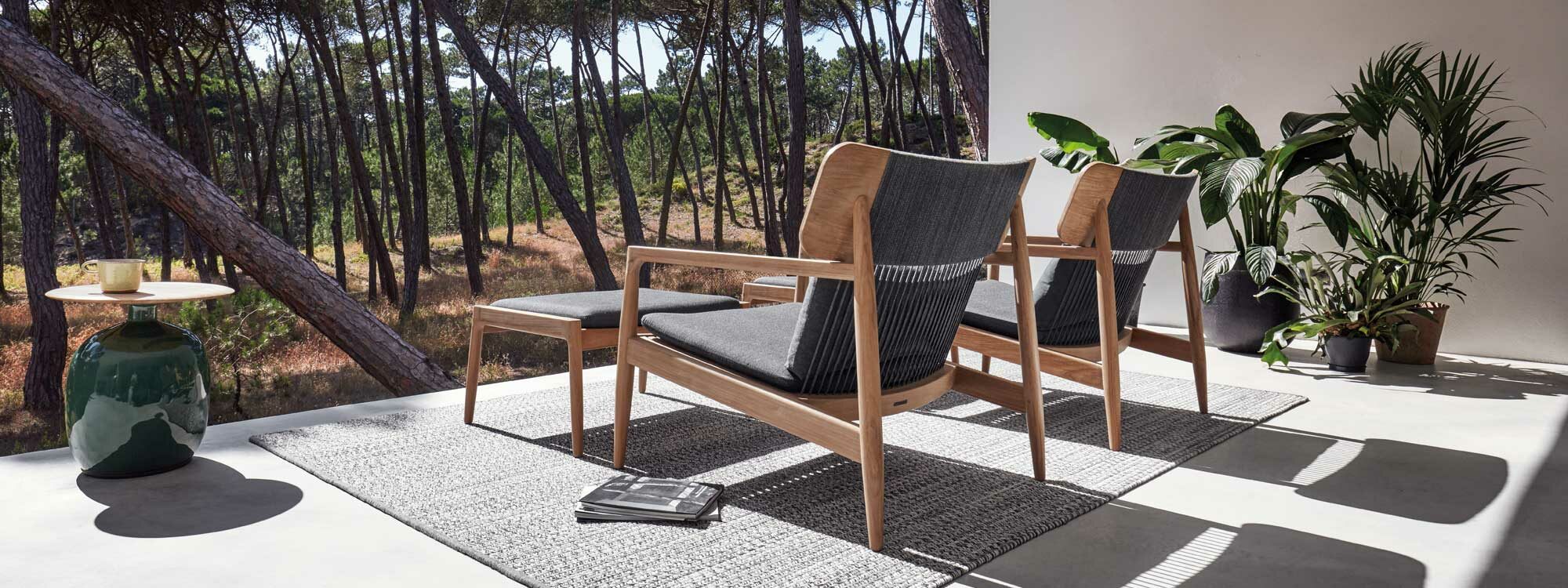 Image of Archi teak lounge chairs and Blow modern low table by Gloster on sunny terrace, with arid woodland in the background