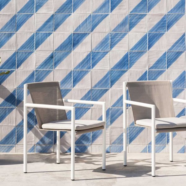 Image of RODA Plein Air white garden chairs against blue and white striped tiled wall in the sunshine