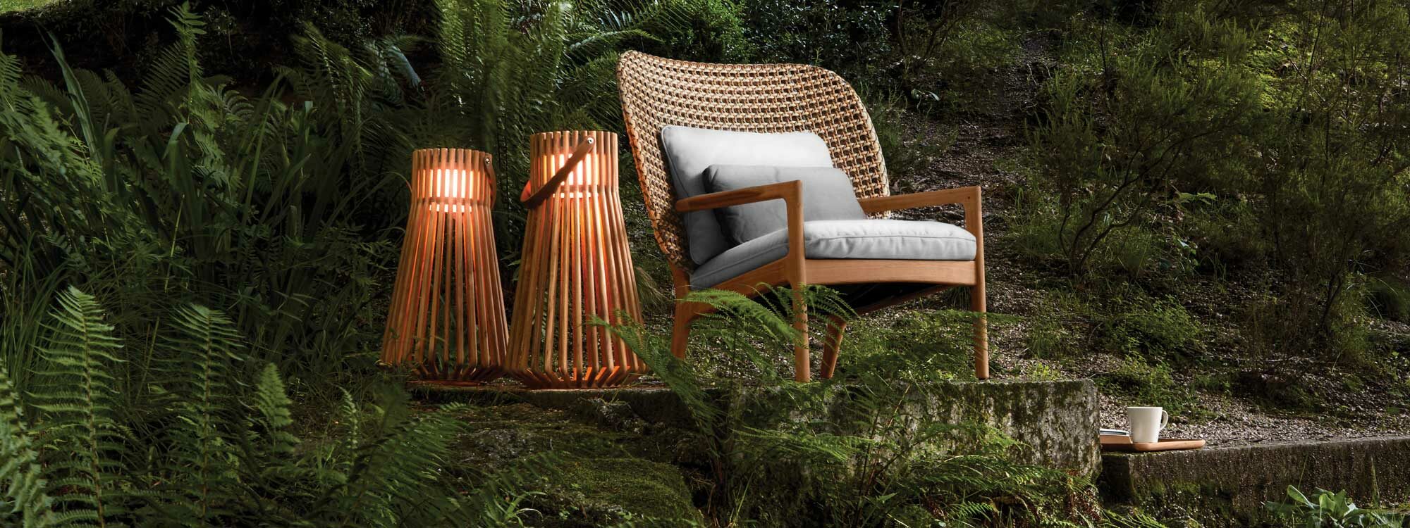 Image of pair of Ambient Ray teak garden lanterns next to Gloster Kay lounge chair