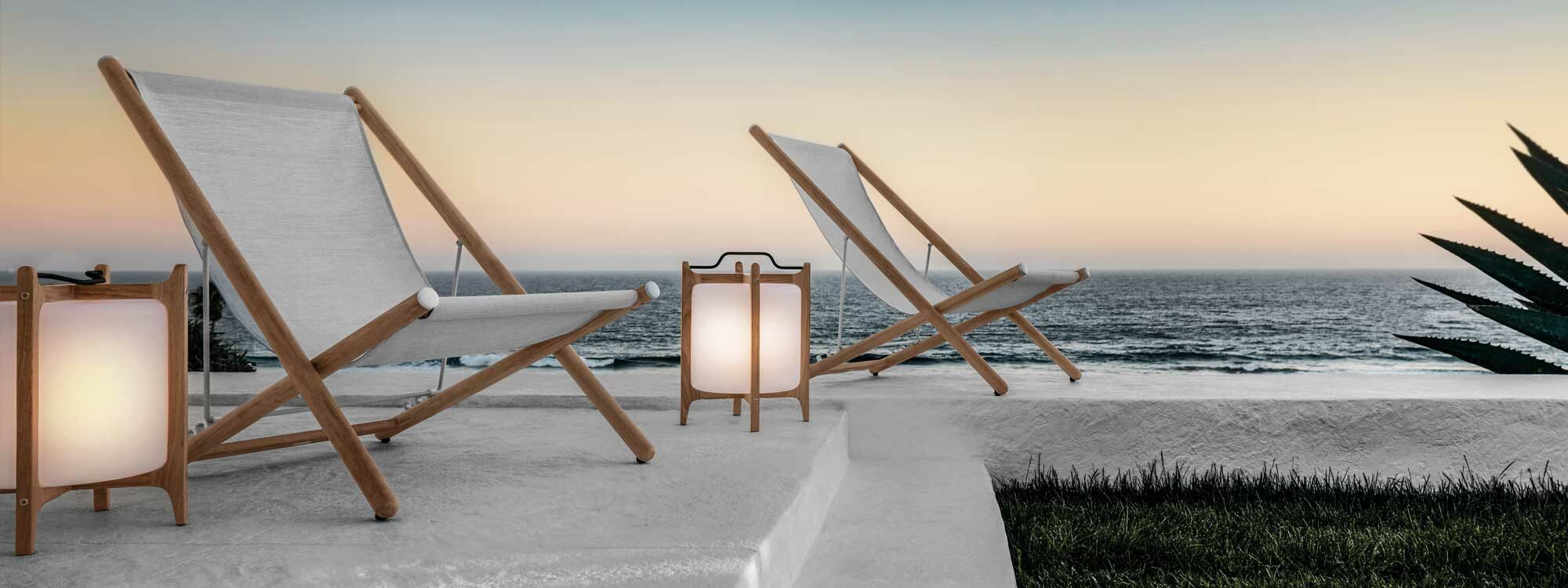Image of lit Ambient Lanterns next to Gloster chairs on beach at dusk