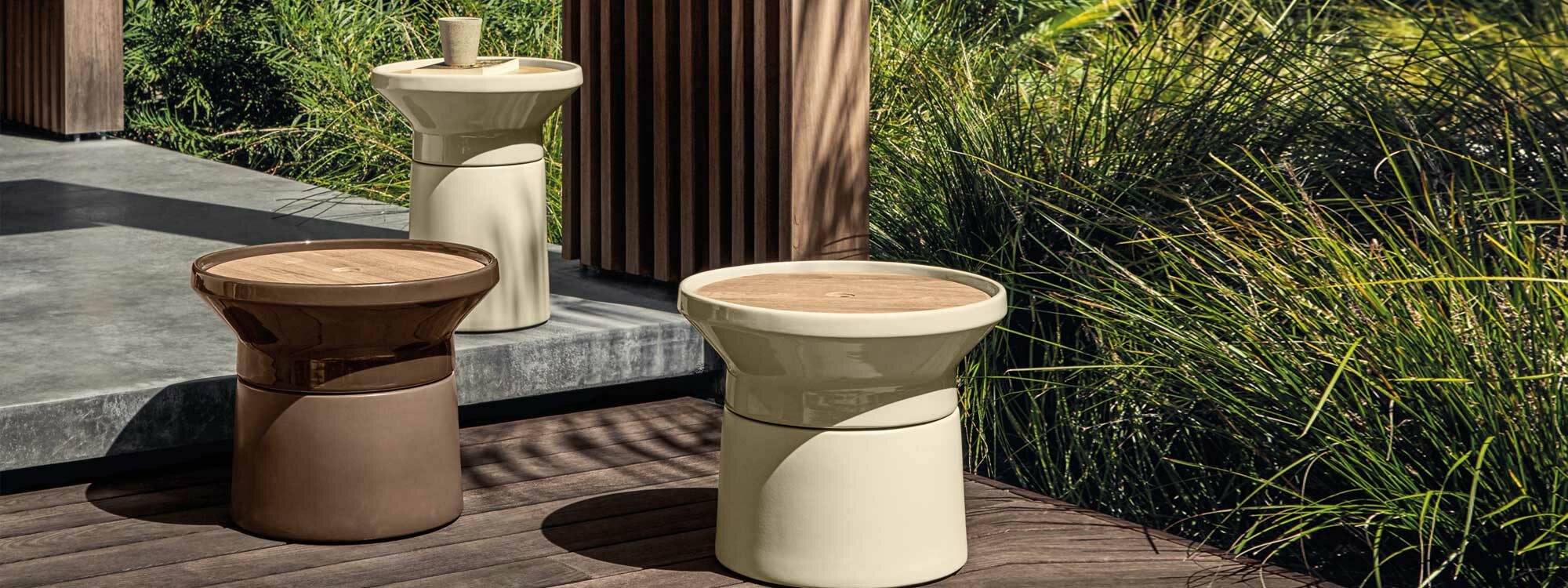 Image of different sizes of Coso outdoor low tables in sand and earth glazed ceramic finishes by Gloster, with architectural grasses in the background