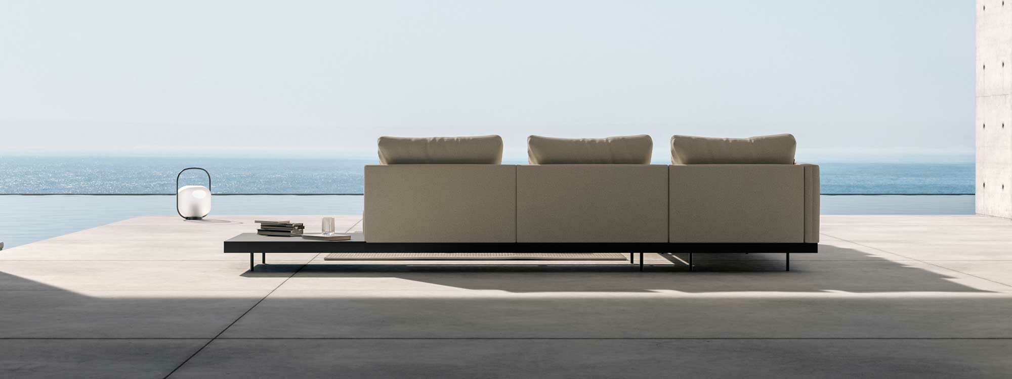 Image of rear of Dongo modern garden sofa by Todus, shown on concrete terrace with blue sea and sky in the background