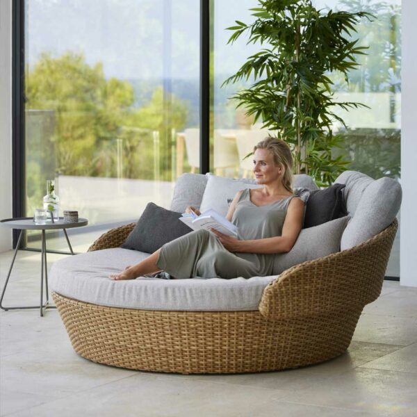Image of woman sat with her feet up, nestling in pile of snug cushions on Cane-line's Ocean Large circular garden daybed