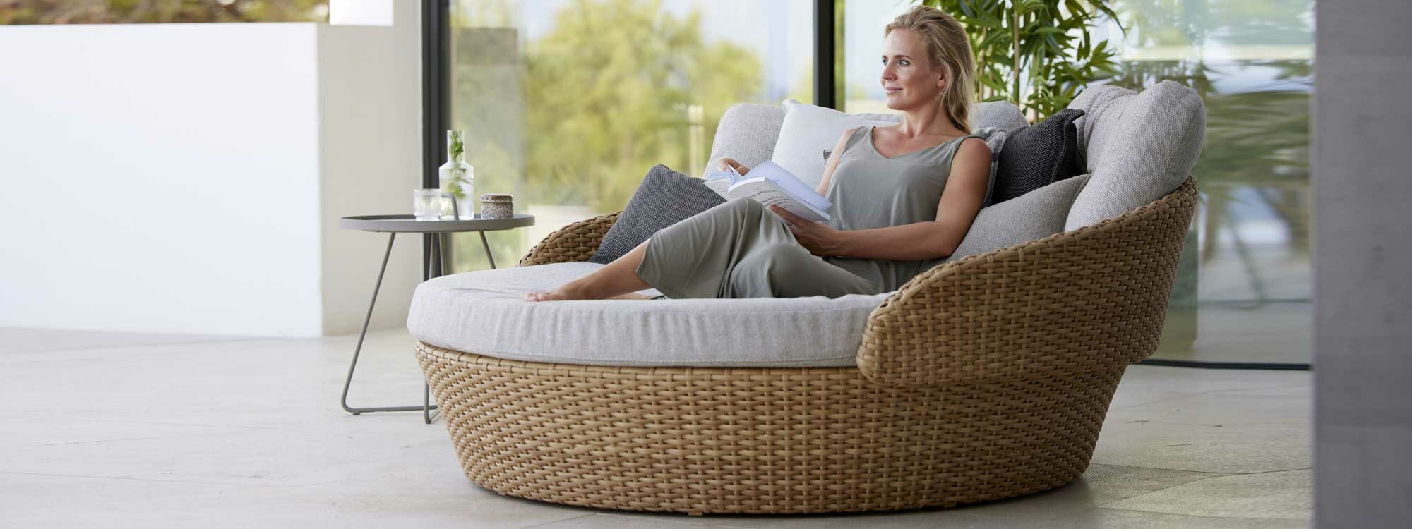 Image of woman sat back with her feet up on Cane-line Ocean large daybed in natural Cane-line Flat Weave with cozy white-grey cushions