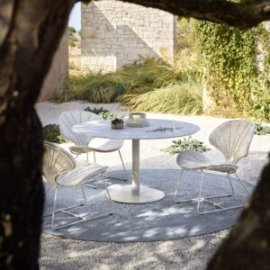 Image of Ostrea minimalist garden chairs and Butler circular dining table beneath the shade of a tree on a sunny terrace
