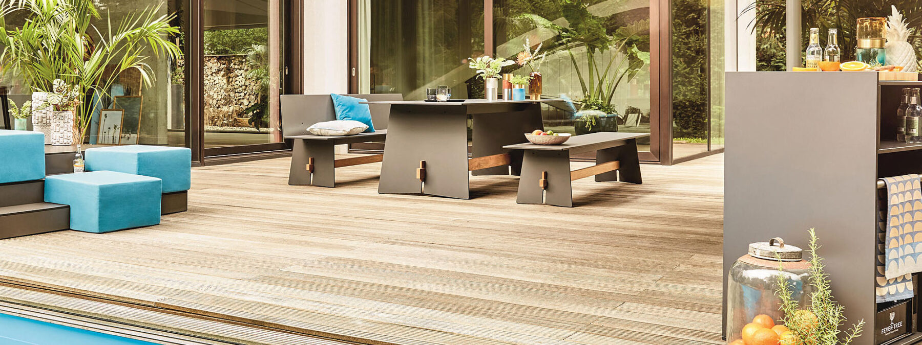 Image of Conmoto Tension dark-grey table and benches on outdoor wooden decking with floor to ceiling glass windows in the background