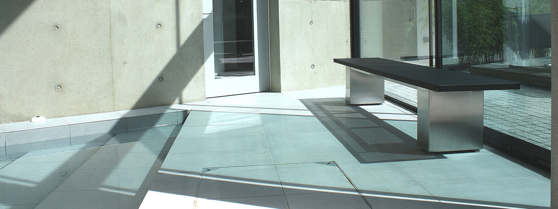 Image of Doble minimalist bench seat with electro-polished stainless steel pedestal bases and black Batyline fabric seat, by FueraDentro