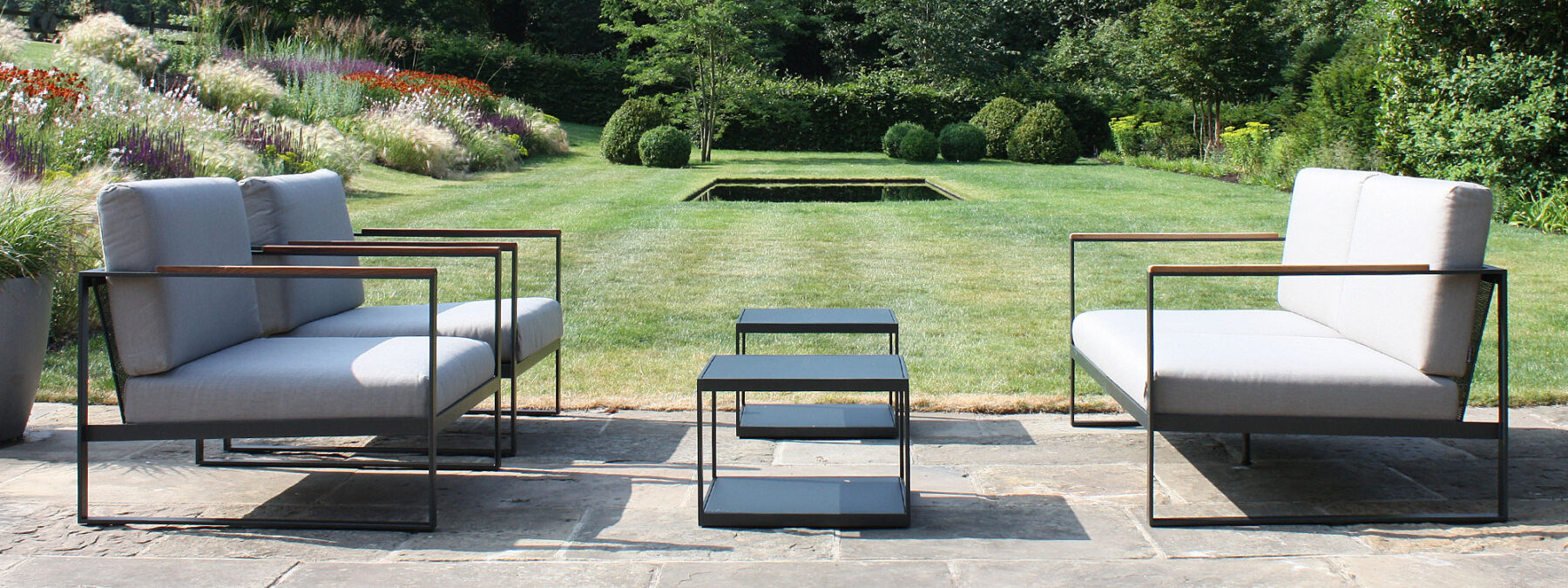 Image of Roshults Garden Easy sofa, lounge chairs and low tables on terrace with beautiful garden in the background in the Meon Valley, Hampshire