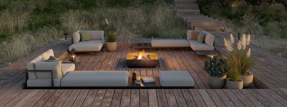 Nighttime image of Royal Botania Alura Lounge corner sofas and twin daybed on recessed wooden decking, surrounded by architectural grasses