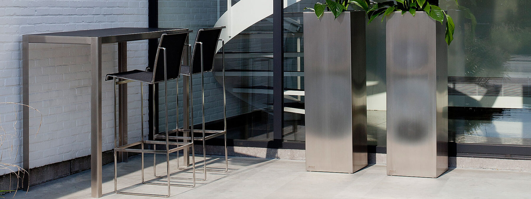 Image of Nimio stainless steel bar table with black ceramic table top and Taburete bar stool with black Batyline seat & back by FueraDentro