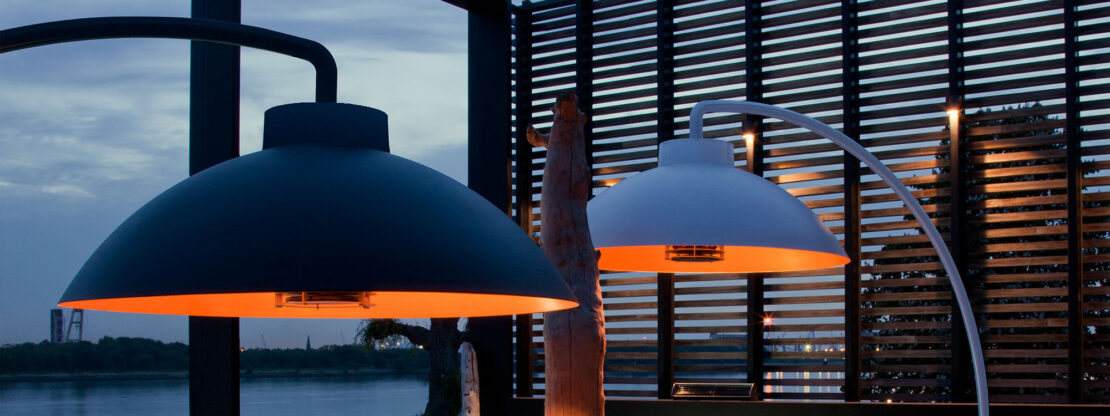 Image of black and white Heatsail Dome patio heaters with louvred fence panel and river in background.