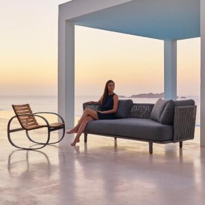 Image of terrace at dusk with woman sat on Moments contemporary garden sofa next to Parc exterior rocking chair by Cane-line