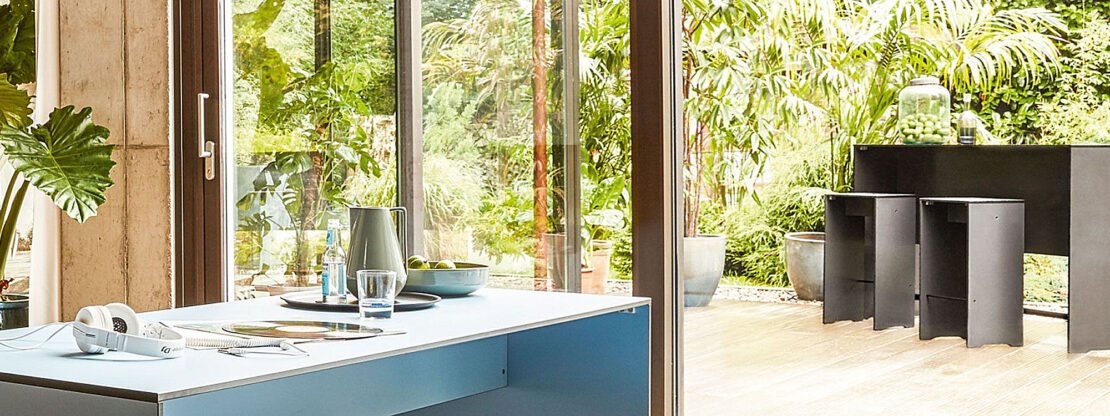 Image of Riva HPL modern table and benches in modern house, with Riva high table and bar stools in anthracite HPL on the terrace outside