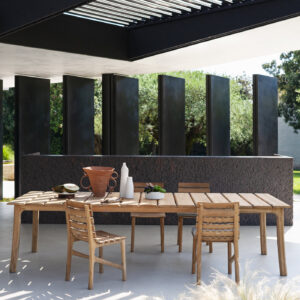 Image of Teseo luxury teak dining table and chairs on poured concrete terrace floor, with brutalist lava console in the background