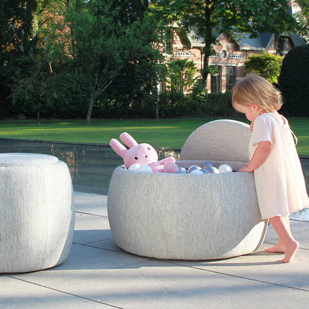 Young girl looking at her toys stored inside Royal Botania Tono garden pouffe & footrest.