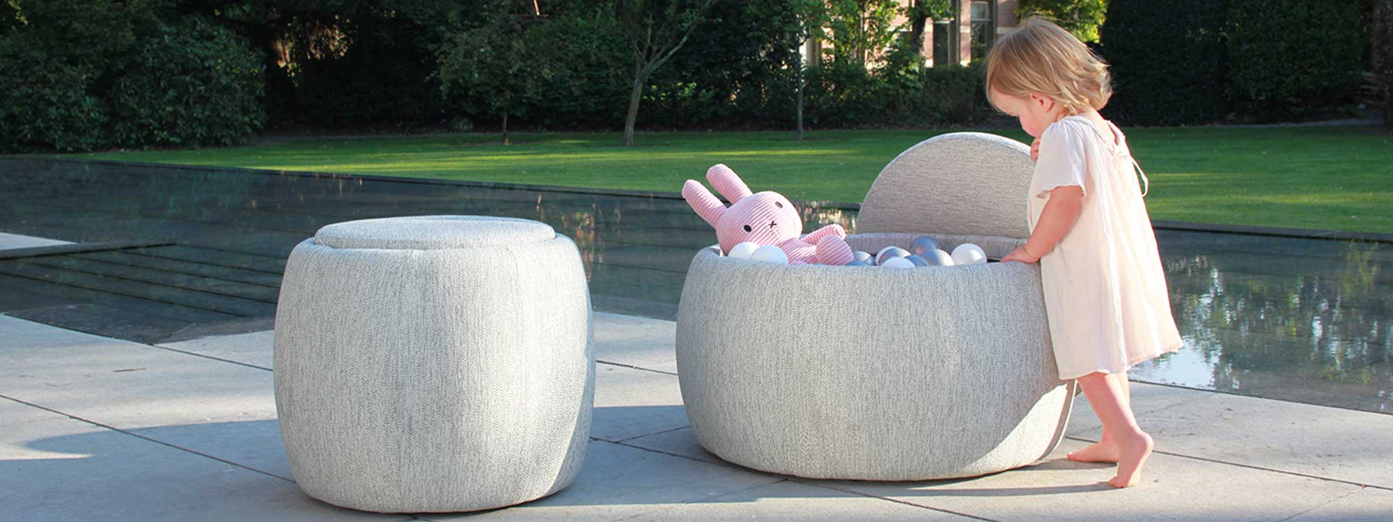 Image of young child lifting lid on Royal Botania Tono pouf to reveal play balls and bunny inside