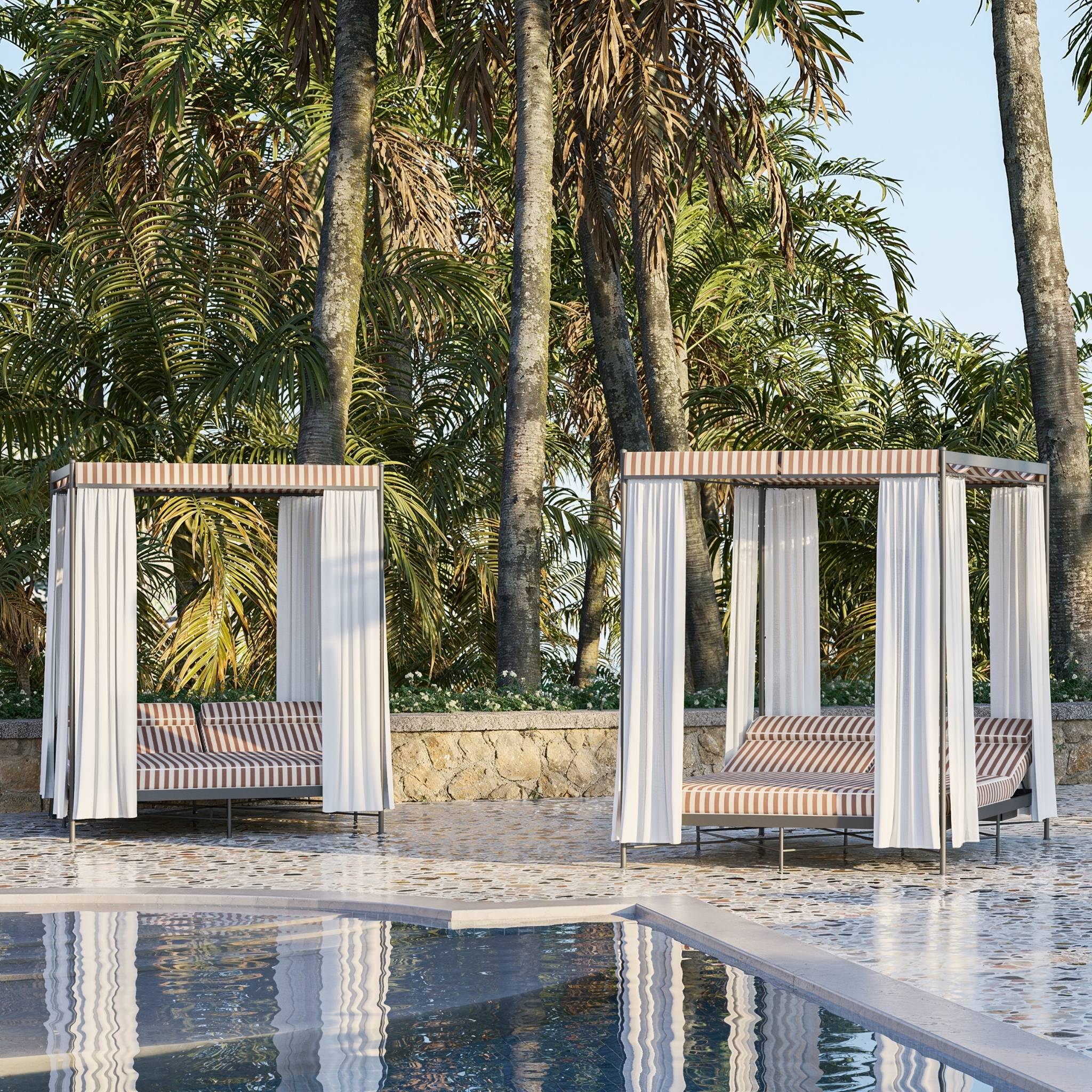 Image of pair of Igea Alcove cabana daybed on poolside with palm trees in the background
